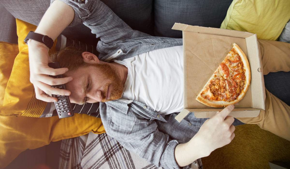 hombre-acostado-en-el-sofa-con-pizza Hombre acostado en el sofá con pizza.